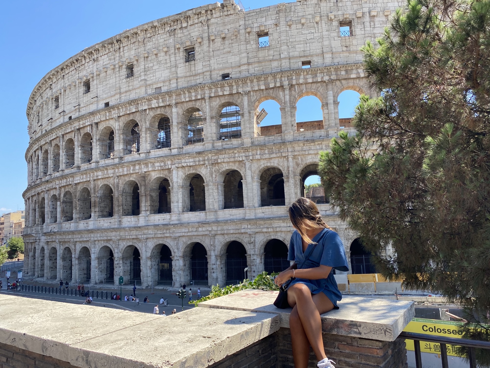 Student sitting outside the Roman Colosseum on a sunny day and facing away from the camera